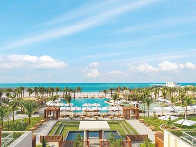 Luxuriöses Resort mit Pool, Palmen und Blick auf das blaue Meer unter blauem Himmel.