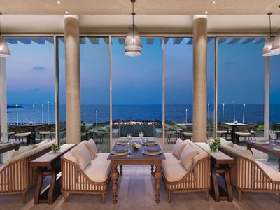 Moderne Hotelbar mit Sitzbereichen und Meerblick bei Dämmerung.