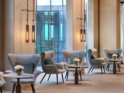 Moderner Sitzbereich mit grauen Sesseln, kleinen Tischen, Blumen und hängenden Leuchten.