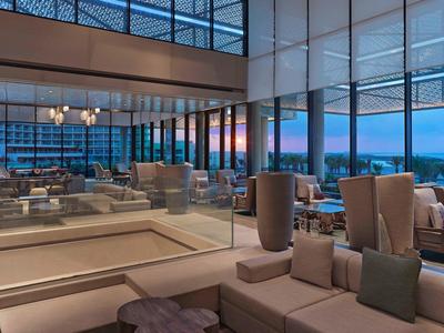 Moderner Wohnzimmerbereich mit großen Fenstern, bequemen Sofas und blau-orange Sonnenuntergangshimmel.