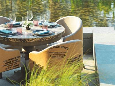 Runder Tisch im Freien mit vier Stühlen und Blick auf Wasser, gedeckt mit Gläsern und Tellern.