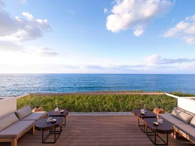 Terrasse mit Sitzmöbeln, Holzboden und Blick auf ruhiges blaues Meer unter blauem Himmel.