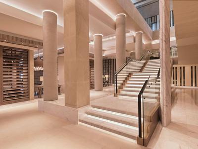 Moderner Hotelinnenraum mit Säulen und beleuchteter Treppe in warmen Beige- und Brauntönen.