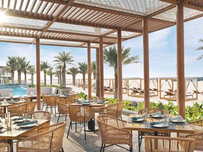 Offenes Restaurant mit Blick auf den Pool, Palmen und Sandstrand bei sonnigem Wetter.