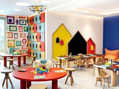 Heller, bunter Kinderraum mit bunten Wänden, kleinen Tischen, Stühlen und Spielelementen.