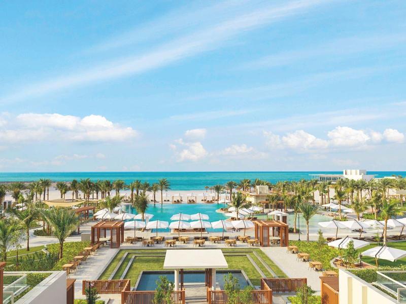 Großer Hotelpool mit Palmen und Blick auf das Meer unter blauem Himmel.