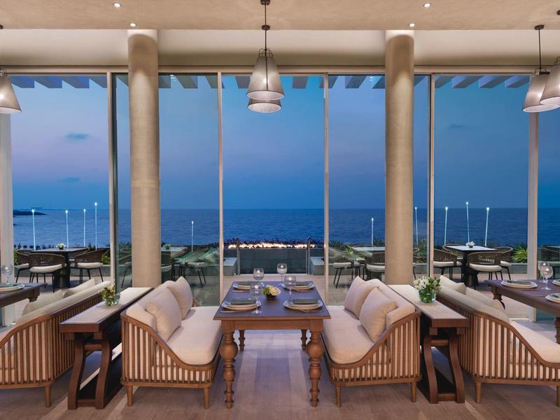 Moderne Hotelbar mit Sitzbereichen und Meerblick bei Dämmerung.