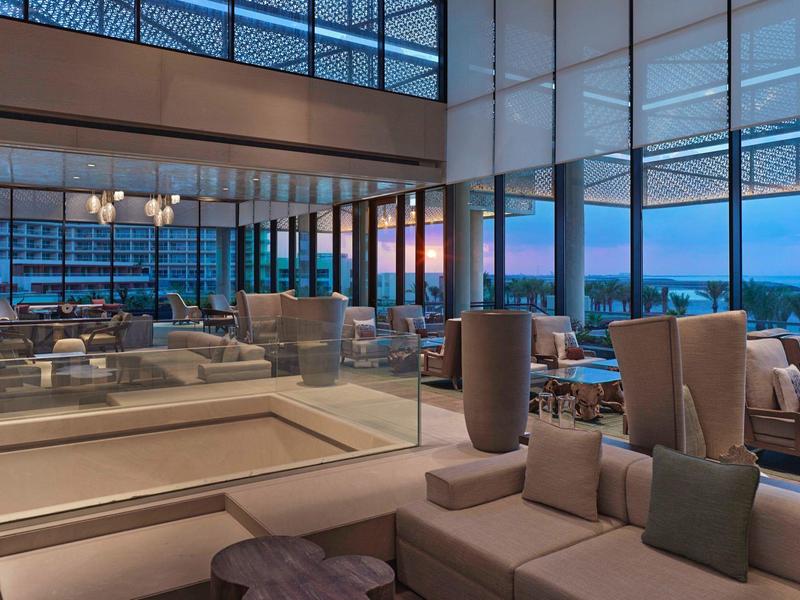 Moderner Wohnzimmerbereich mit großen Fenstern, bequemen Sofas und blau-orange Sonnenuntergangshimmel.