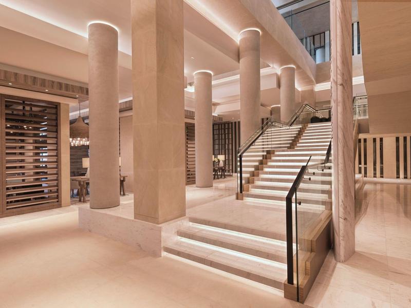 Moderner Innenraum mit heller Holztreppe, Säulen und großzügigem, minimalistischem Design.