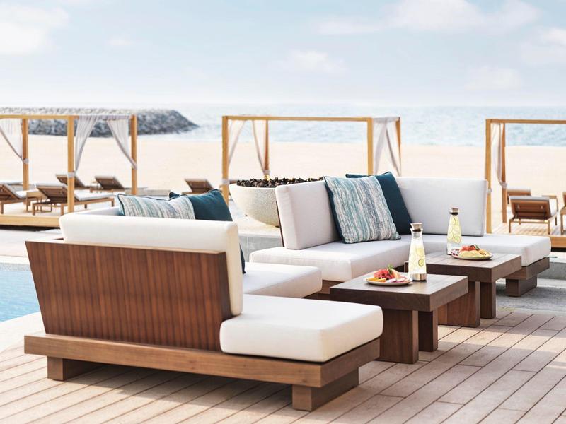 Moderner Außenbereich mit weißen Polstersofas, Holzmöbeln und Pool im Hintergrund.