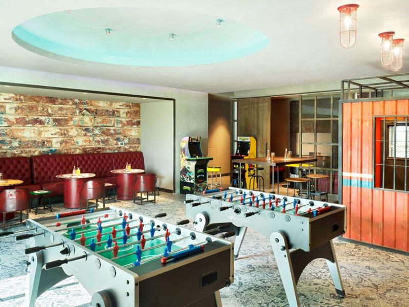 Moderne Spielhalle mit Tischfußball und Lounge-Bereich, helle Beleuchtung und bunte Möbel.