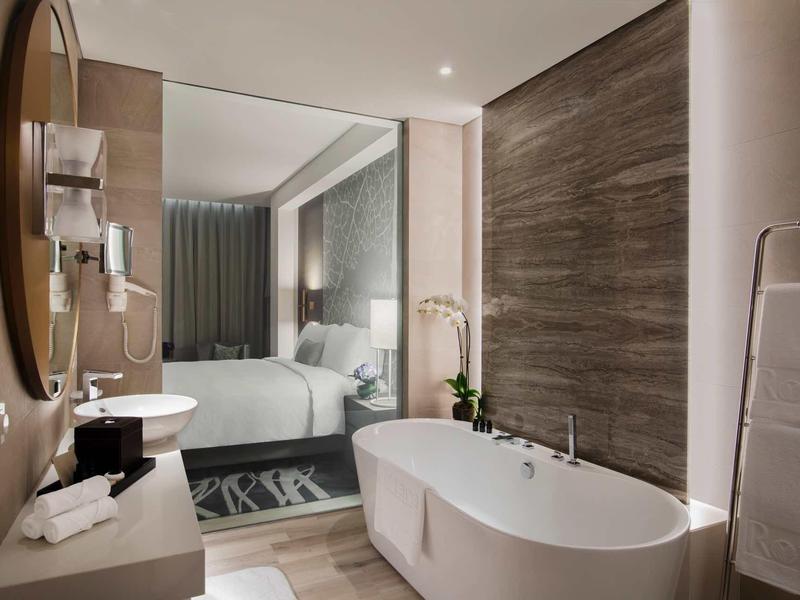 Modern hotel bathroom with freestanding bathtub and transparent wall to bedroom.