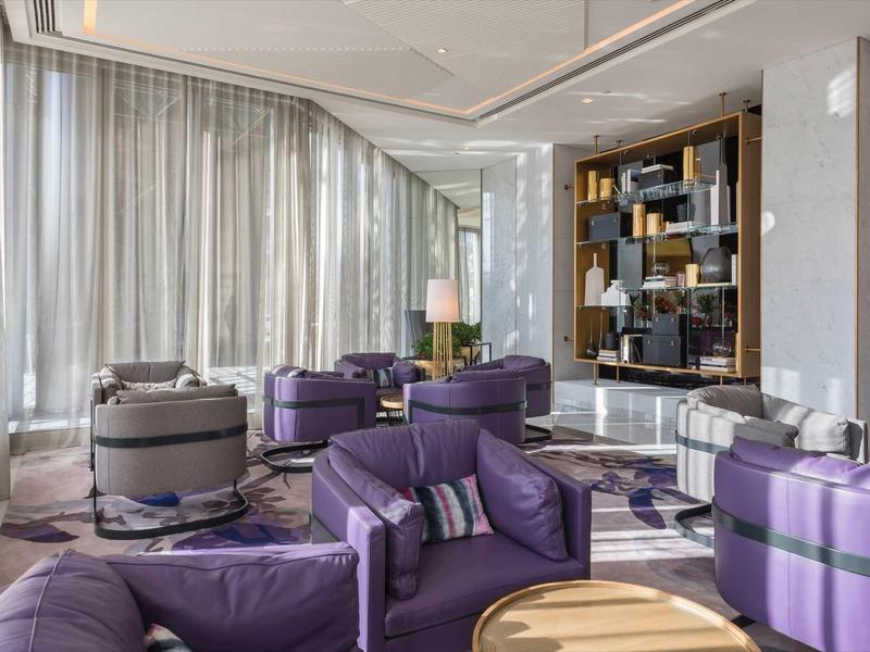 Modern hotel lounge area with purple armchairs and large windows.