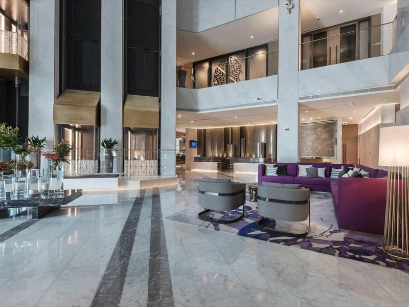 Spacious hotel lobby with modern seating areas, marble floors, and tall windows.