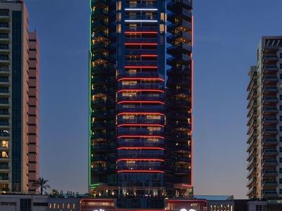 Hohes modernes Gebäude mit Lichtschmuck und roter Beleuchtung, nachts vor dunklem Himmel.