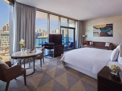 Modernes Hotelzimmer mit großem Bett, Sitzbereich, bodentiefen Fenstern und Stadtblick.