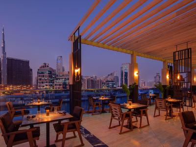 Modernes, offenes Restaurant mit Holzmöbeln, warmem Licht und Blick auf beleuchtete Stadt bei Dämmerung.