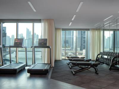 Siłownia z bieżniami i hantlami przed dużymi oknami z widokiem na miasto.