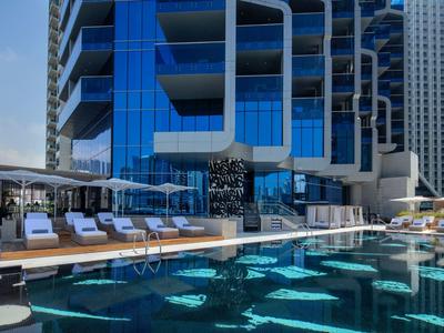 Moderner Außenpool mit Liegestühlen und Glasfassade eines Hochhauses im Hintergrund.