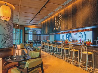 Modernes Restaurant mit Bartresen, Holzstühlen, warmem Licht und asiatischer Wanddekoration.