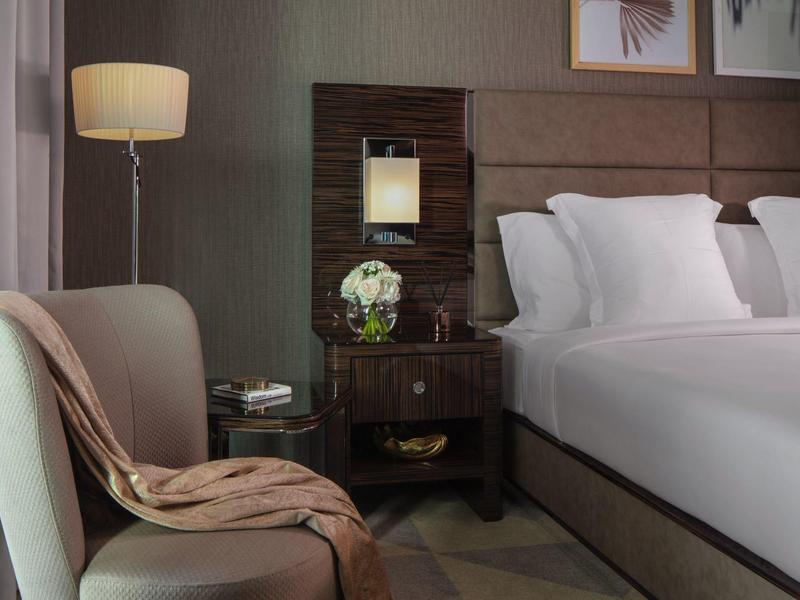 Modernes Schlafzimmer mit großem Bett, Nachttisch, Stehlampe und einem hellen Sessel mit Decke.