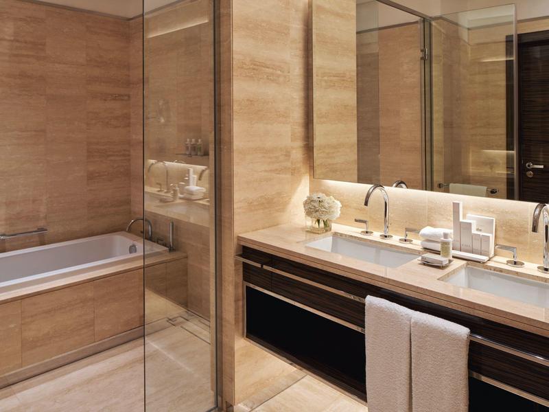 Modernes Badezimmer mit Holzfliesen, großer Badewanne, Doppelwaschbecken und Spiegelwand.