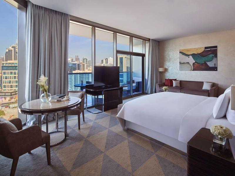 Modernes Hotelzimmer mit großem Bett, Sitzbereich, bodentiefen Fenstern und Stadtblick.