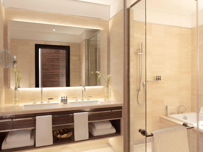 Modernes Badezimmer mit Doppelwaschbecken, großer Spiegel, Glasdusche und Badewanne in warmen Beige- und Brauntönen.