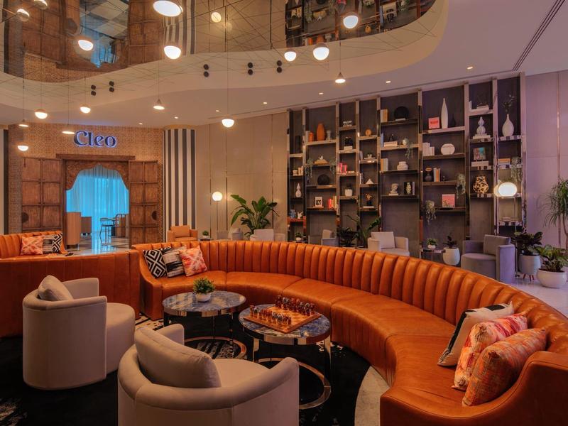 Moderne Lounge mit oranger, geschwungener Sofa, grauen Sesseln, Regalen und warmem Licht.