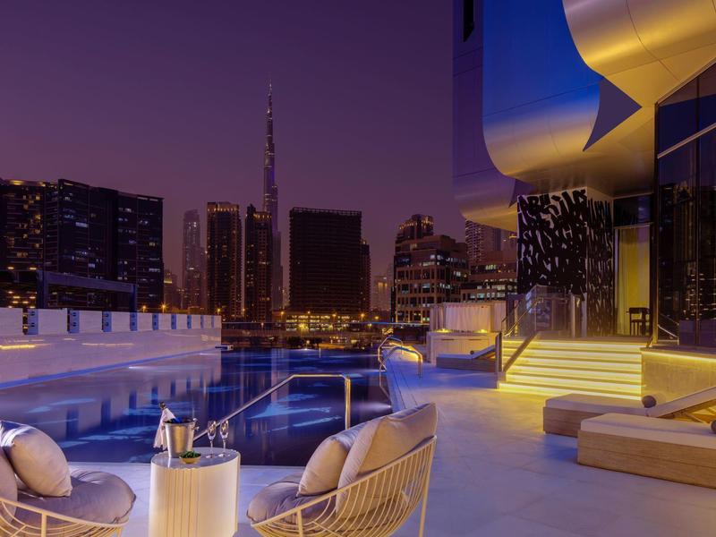 Luxuriöse Dachterrasse mit Pool und Sitzbereich, moderne Stadtlichter im Hintergrund bei Abenddämmerung.