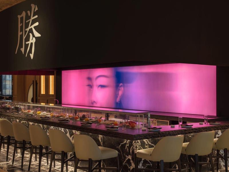 Moderner Sushi-Bar mit rosa beleuchtetem Thekenbereich und bequemen Stühlen in elegantem Ambiente.