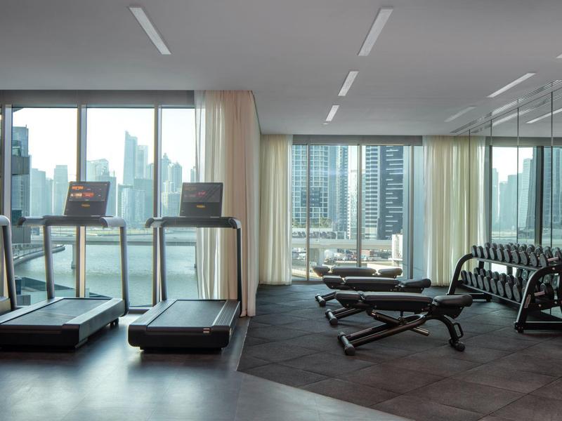 Helles Fitnessstudio mit Laufbändern, Hanteln und großer Fensterfront mit Stadtblick.