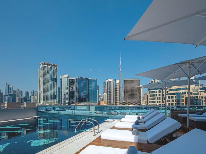 Dachpool mit Liegestühlen und moderner Stadt-Skyline vor klarem Himmel bei Tageslicht.