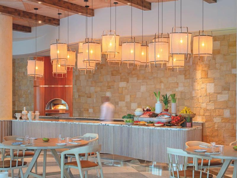 Moderner Gastraum mit hängenden gelben Lampen, Rundtischen, Stühlen und Buffet mit Speisen.