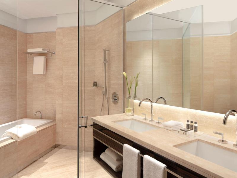 Modernes Badezimmer mit beigem Fliesen, Doppelwaschbecken und Glasdusche, Badewanne in Ecke.