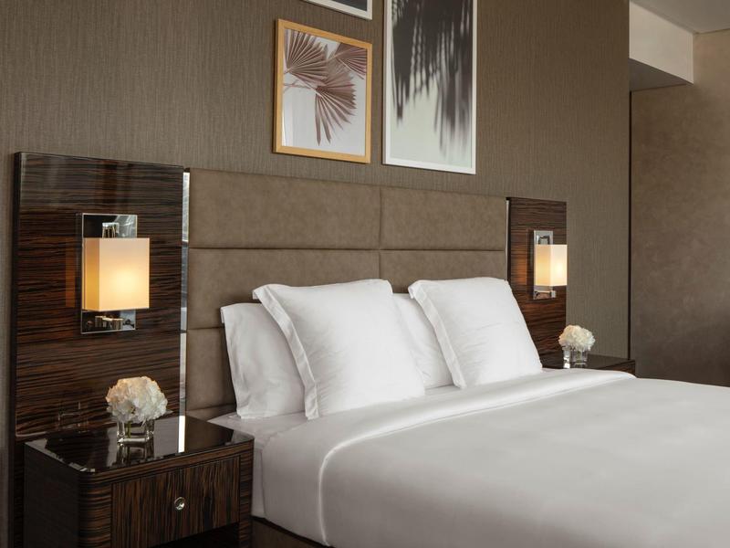 Modernes Schlafzimmer mit braunem Kopfteil, weißen Kissen, Nachttischen und warmen Wandlampen.