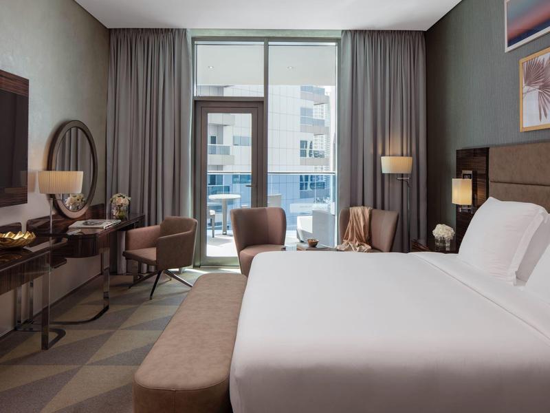 Modernes Hotelzimmer mit großem Bett, Sitzbereich, TV, Schreibtisch und Balkon mit Stadtblick.