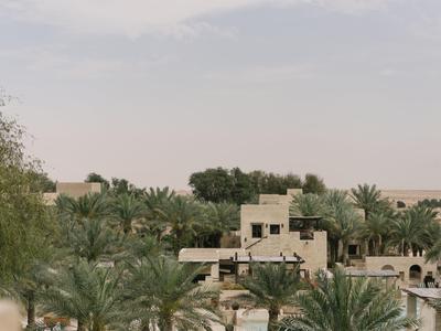 Bright desert resort with sand-colored buildings and palm trees under a cloudy sky.