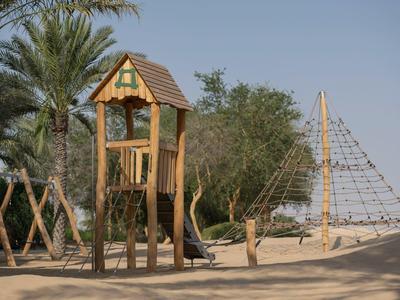 Sandy playground with wooden climbing structure and palm trees in the background.