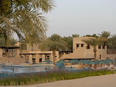Hotel pool with lounge chairs and buildings in a sunny desert setting with palm trees.