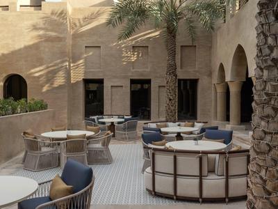 Outdoor terrace with modern seating in front of a building with arches and a palm tree.