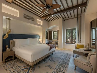 Bright hotel room with wooden ceiling beams, large bed, and seating area with rug.