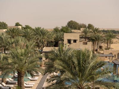 Hotelcomplex met zwembad en palmbomen in een woestijnomgeving onder een bewolkte lucht