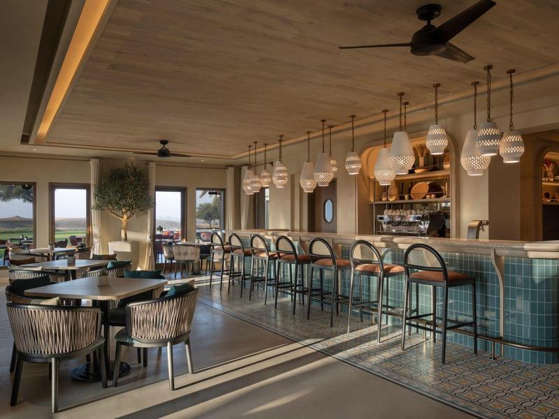 Elegant hotel bar with high stools, modern lighting, and wide views through large windows.