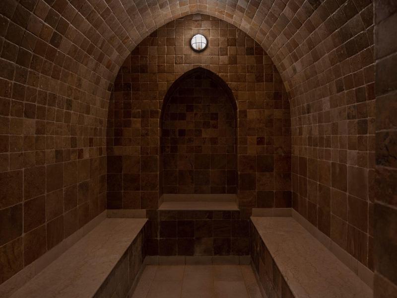 Dark mosaic steam room with two benches and a clock above an arch