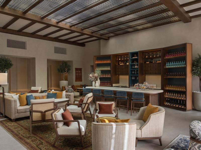 Elegant hotel lounge with sofas, armchairs, and a bar with shelves full of wine bottles.