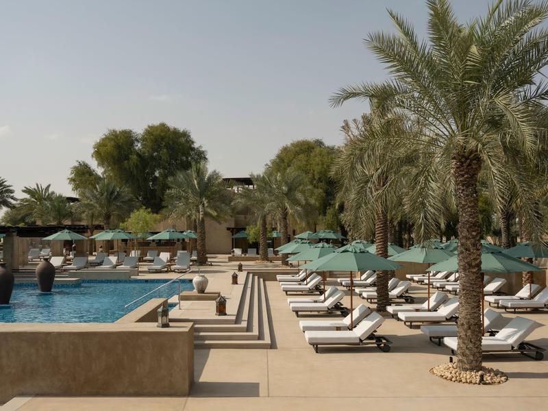 Luxury hotel pool with sun loungers and palm trees under a clear sky.