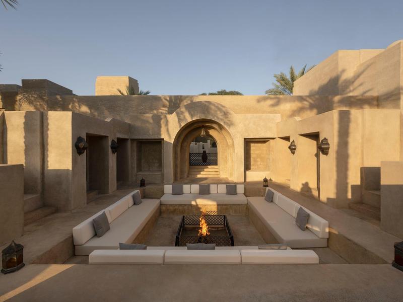 Seating area with fire pit in a sandy-colored courtyard under clear sky.