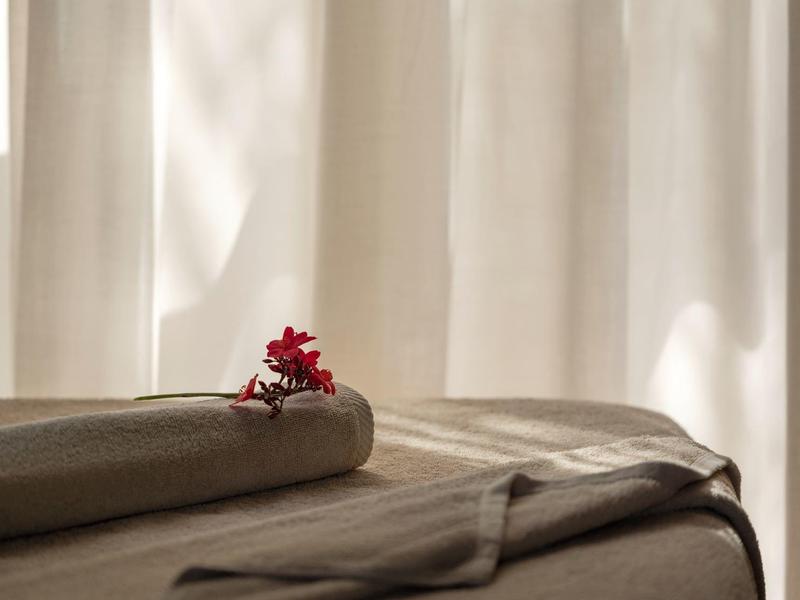 Soft daylight falls on a welcoming spa bed draped with towels and adorned with a red flower.