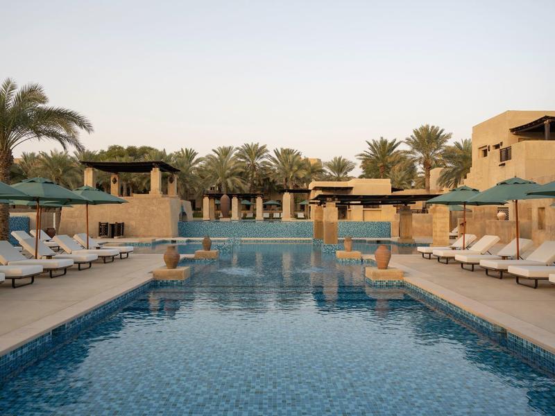 Large outdoor pool with sun loungers and palm trees at a luxury hotel resort.